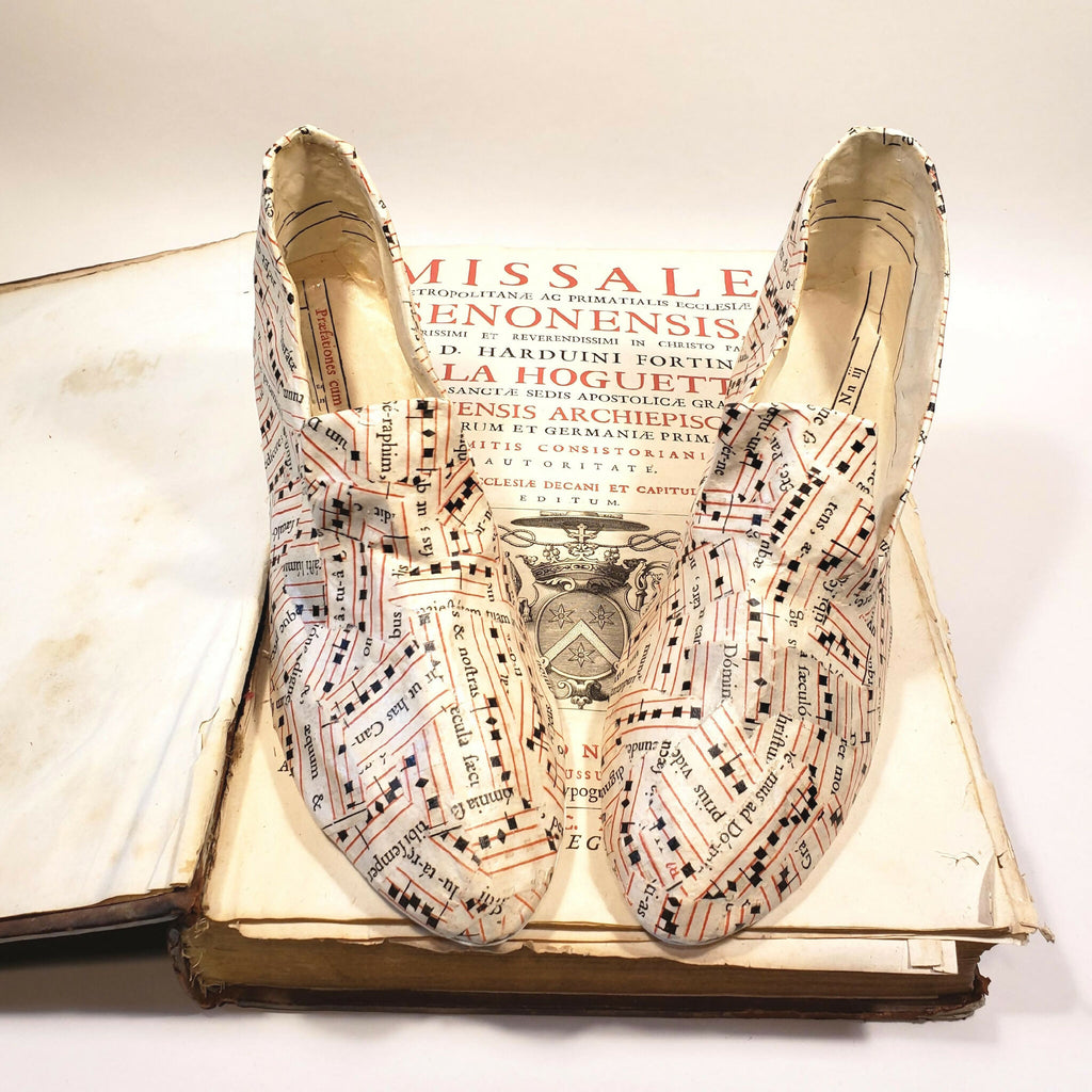 Escarpins beige à motif imprimé, posés sur une page de livre ancienne, bout pointu.