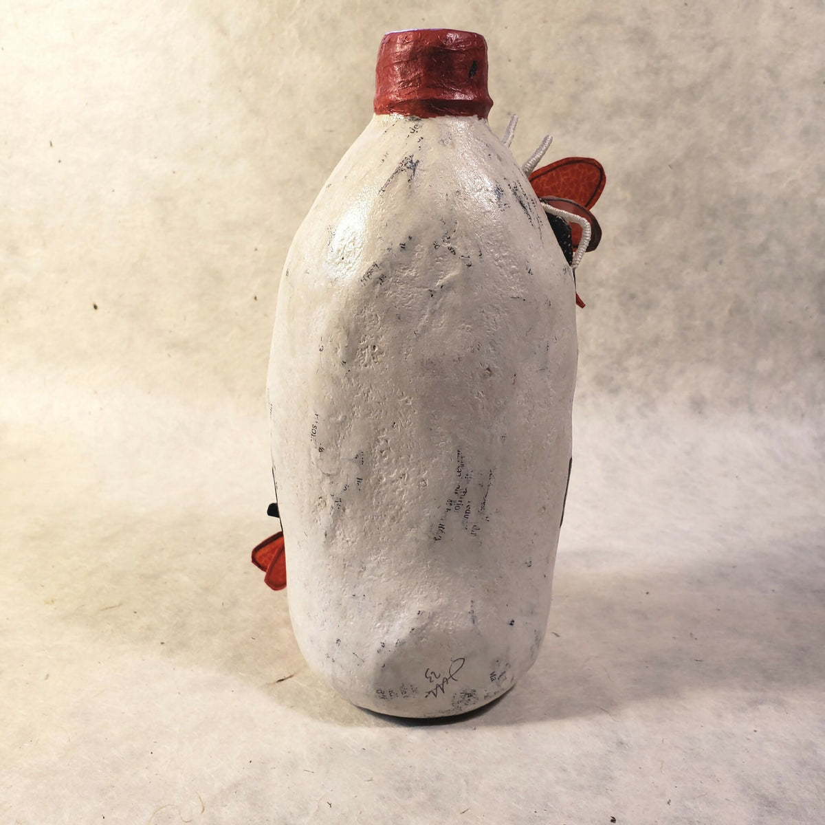 Sculpture de bouteille blanche avec chapeau rouge, vue arrière avec petits éléments rouges