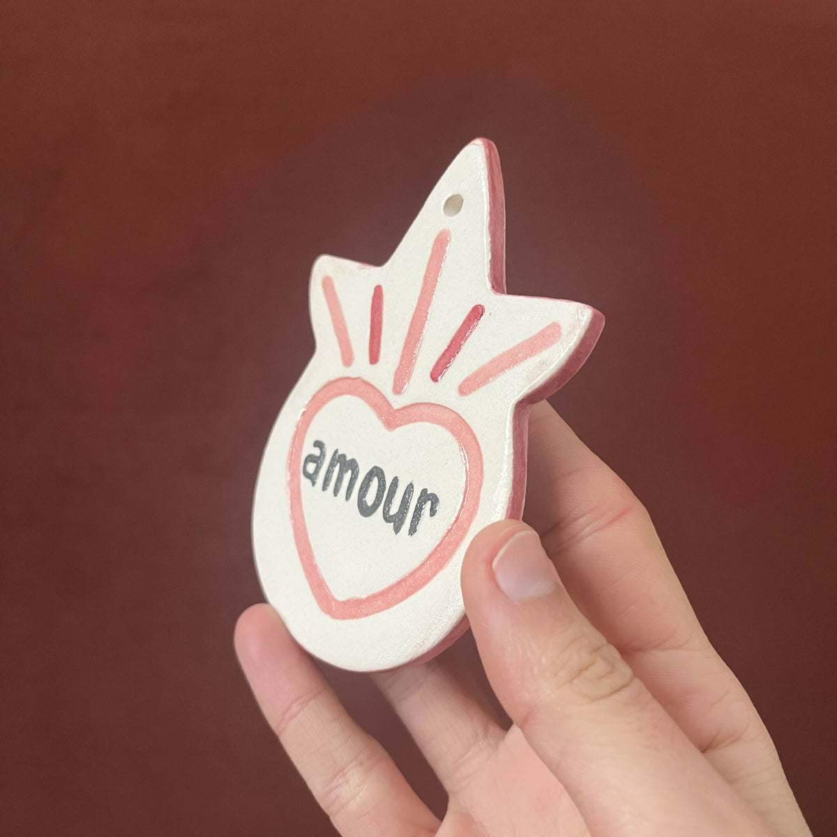 Ex-voto en forme d’étoile, texte « amour » dans un cœur rouge sur fond blanc cassé.