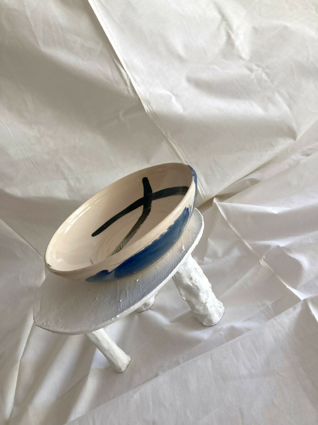 Bol en grès blanc avec motif bleu en croissant, vue en biais sur pied.