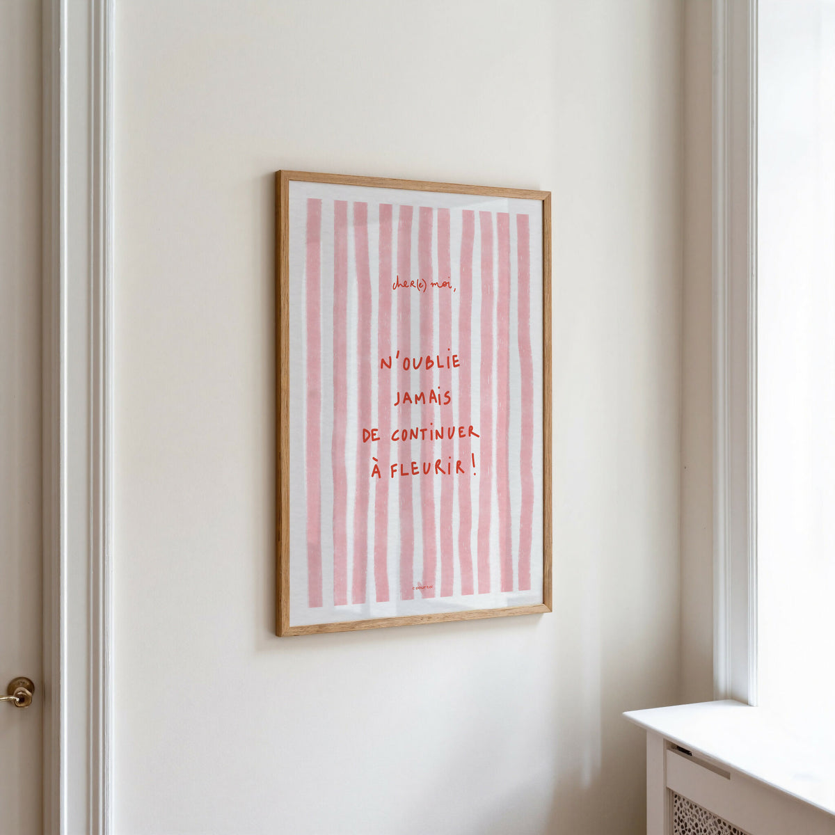 Affiche encadrée sur mur, rayures verticales roses et citation manuscrite « À fleurir »