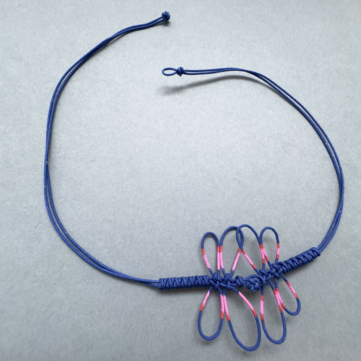 Bracelet bleu avec motif de libellule rose en frange de cordelettes, fermoir ajustable.