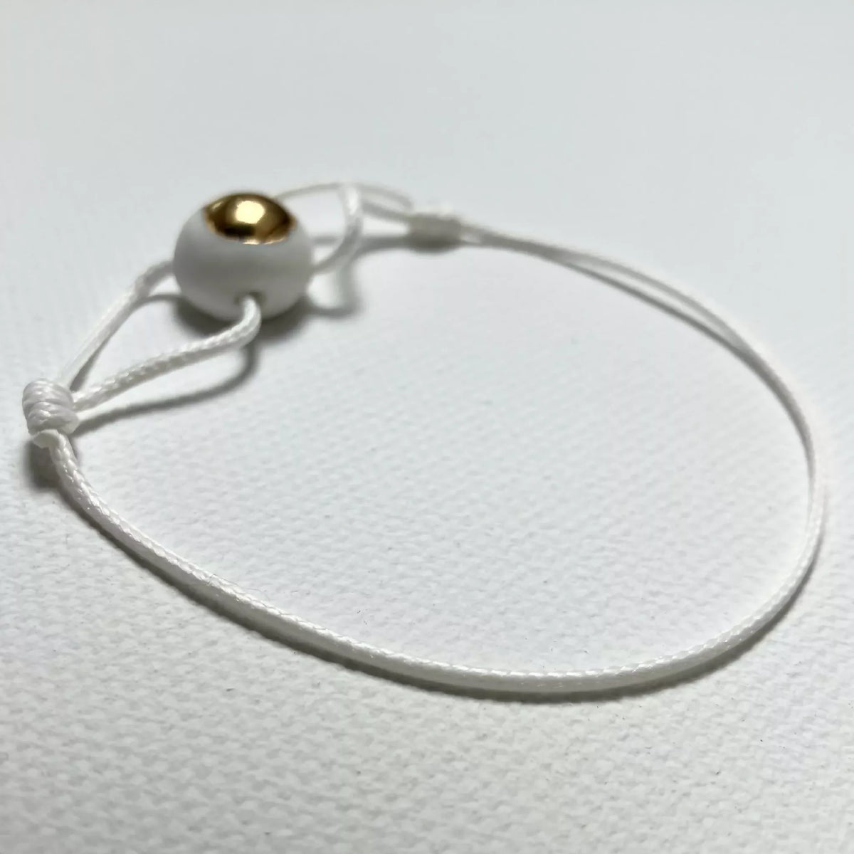 Bracelet en cordon blanc avec perle dorée et attache
