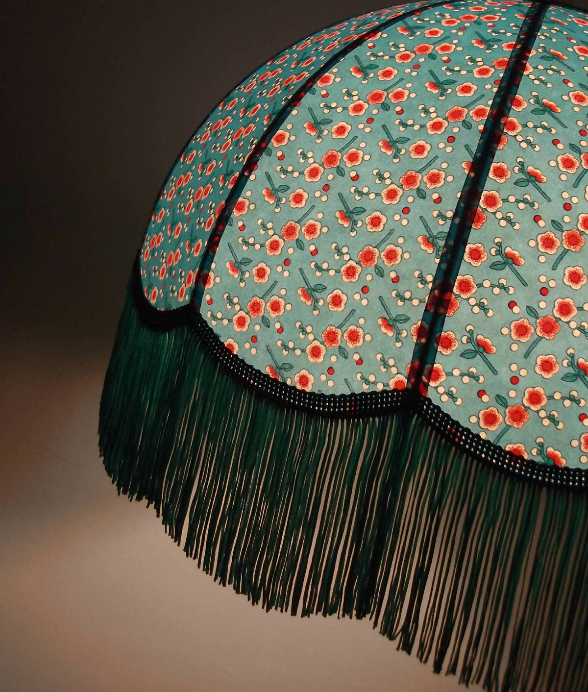 Abat-jour papier bleu motifs fleuris, bordure noire et franges vertes détaillées.