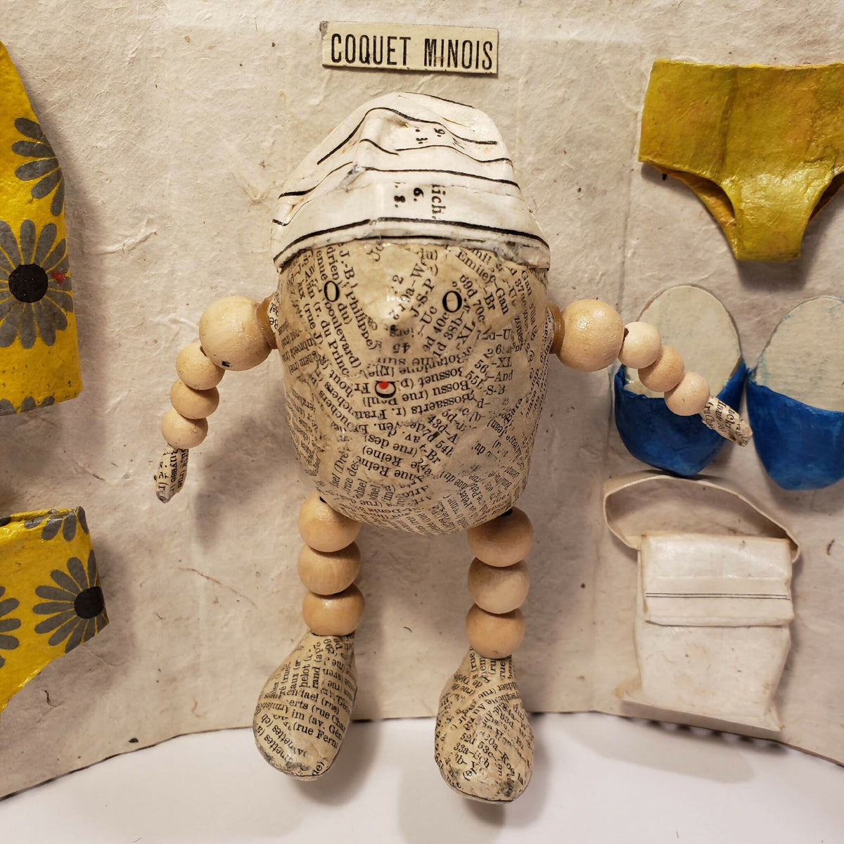 Sculpture Coquet minois : figurine en tissu beige, détails imprimés et accessoires