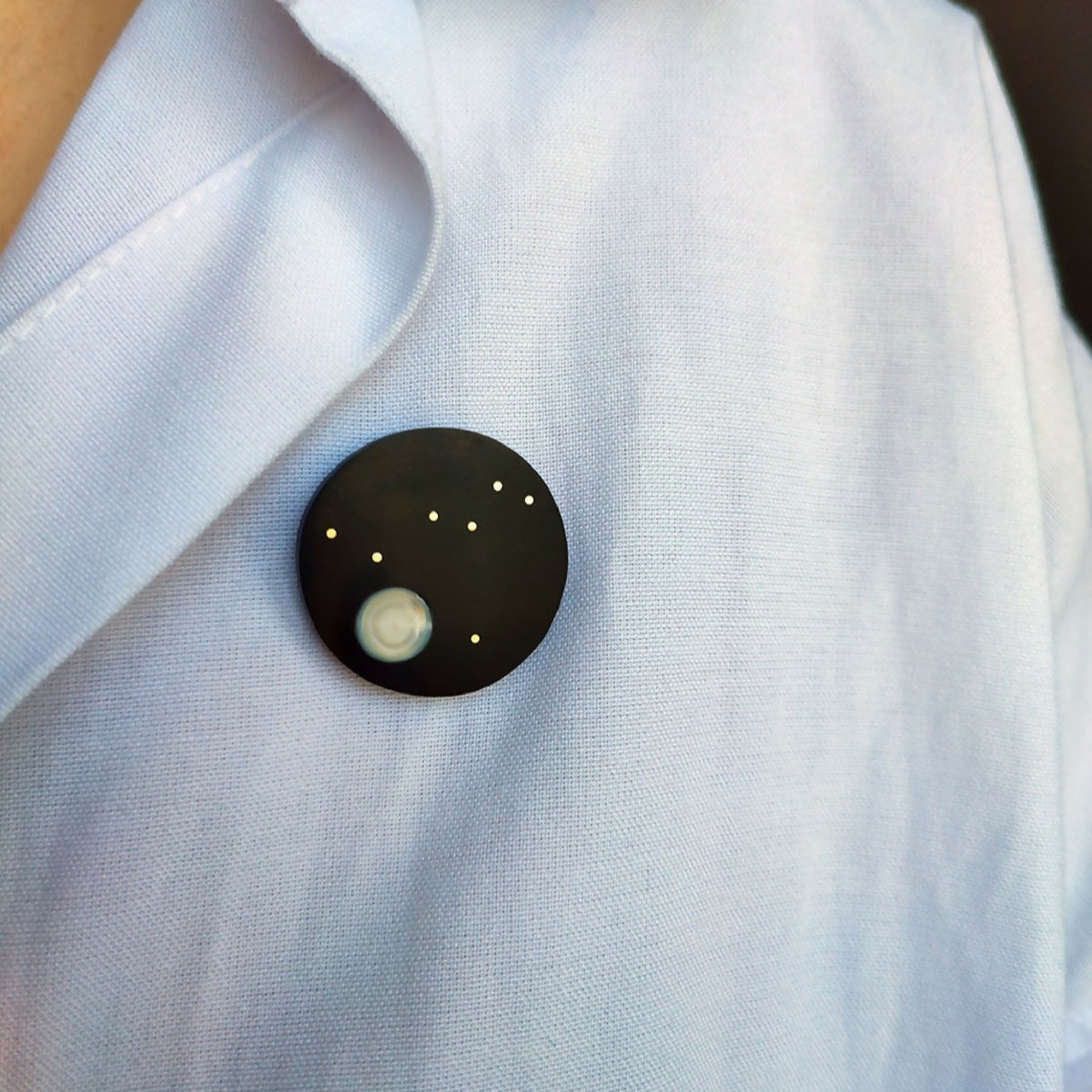 Broche Columba sur chemise claire: cercle noir, ovale clair et points dorés