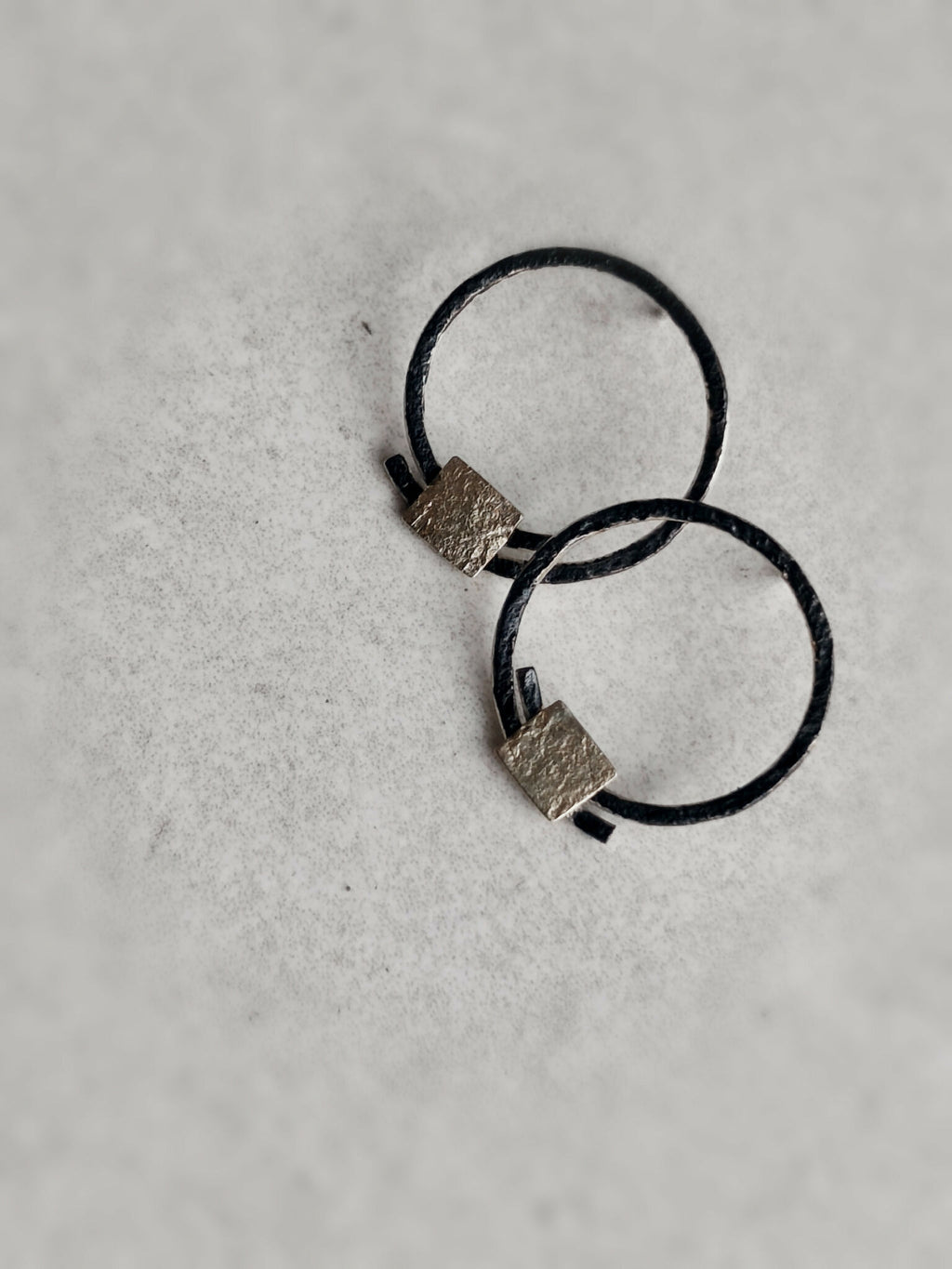 Boucles d’oreilles anneaux noirs, carrés texturés dorés, position croisées