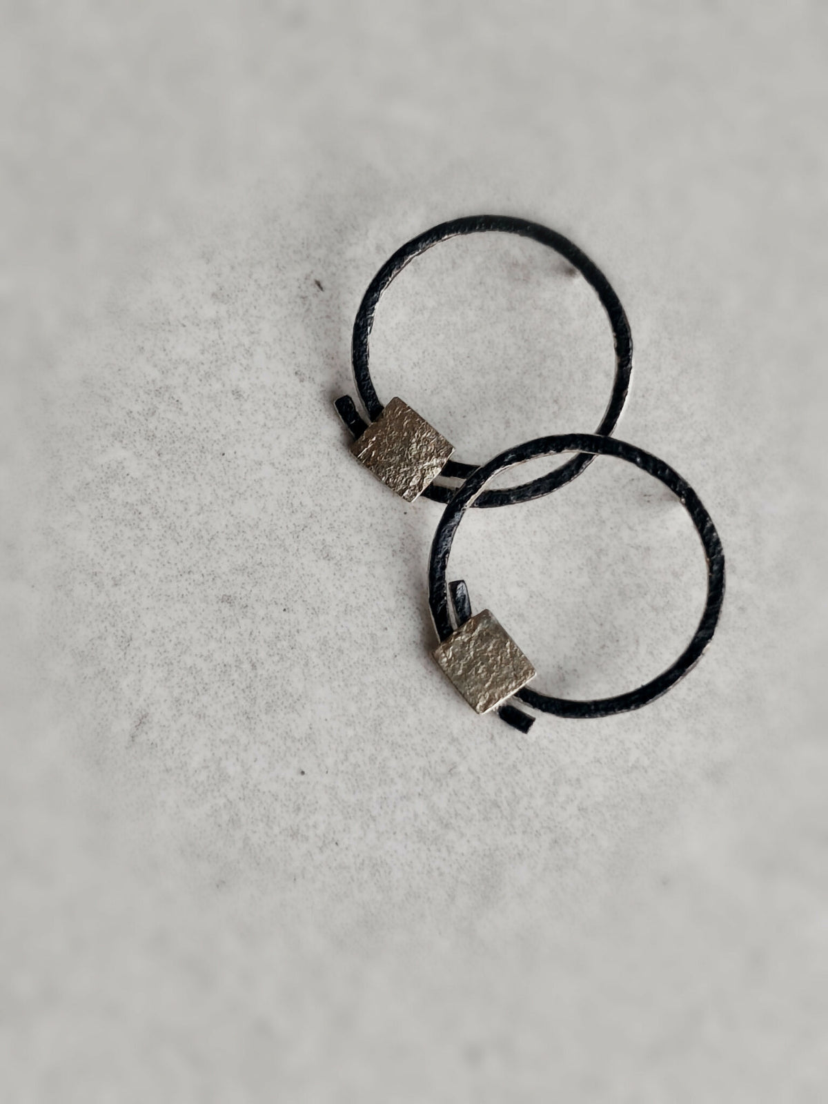 Boucles d’oreilles anneaux noirs, carrés texturés dorés, position croisées