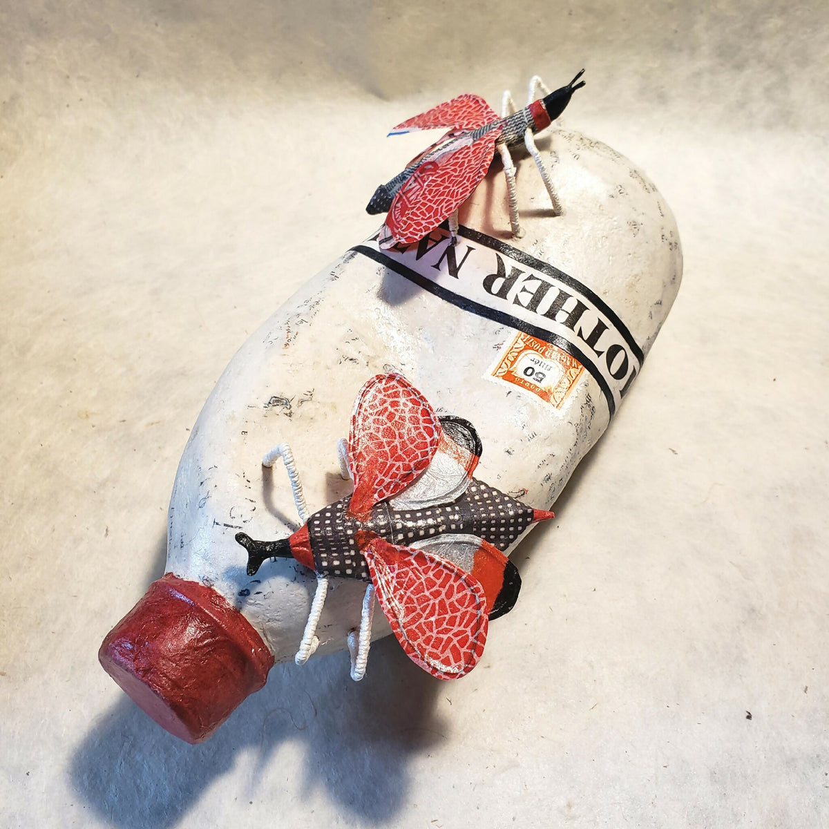 Sculpture de bouteille blanche chapeau rouge, papillons rouges et ruban noir autour