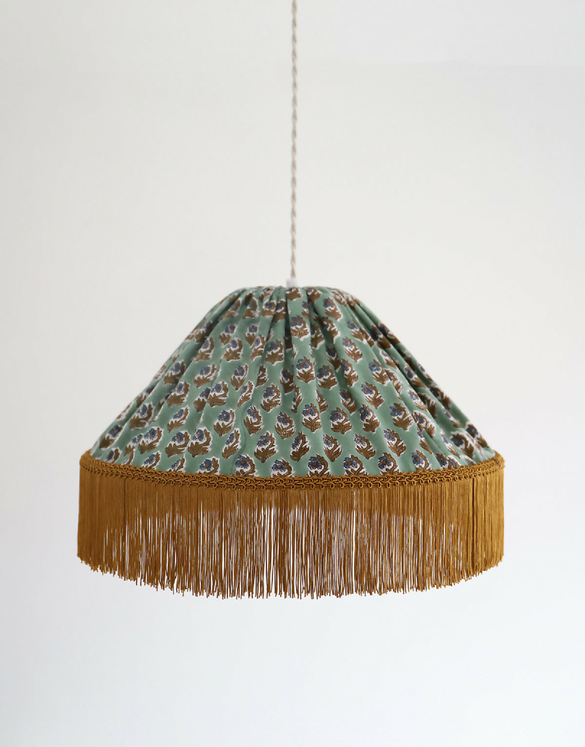 Abat-jour de suspension en tissu vert à motifs floraux, frange dorée au bas.