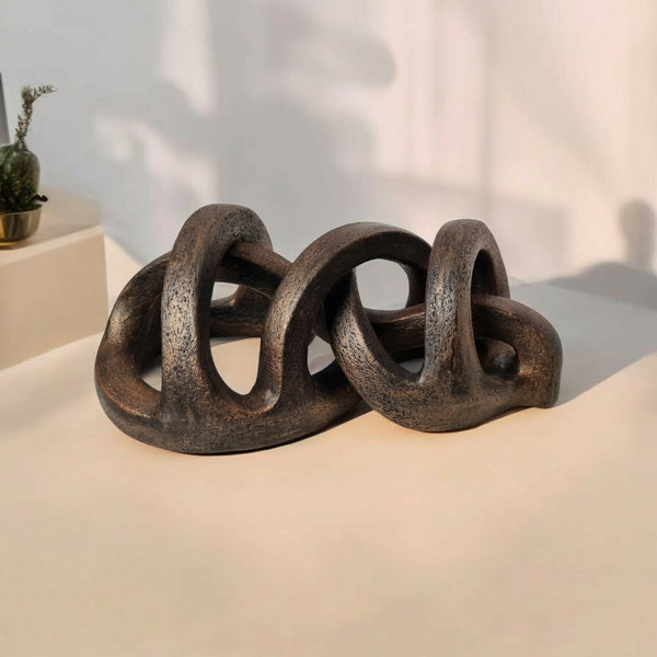 Sculpture abstraite en argile sombre sur socle, arches et anneaux entrelacés.