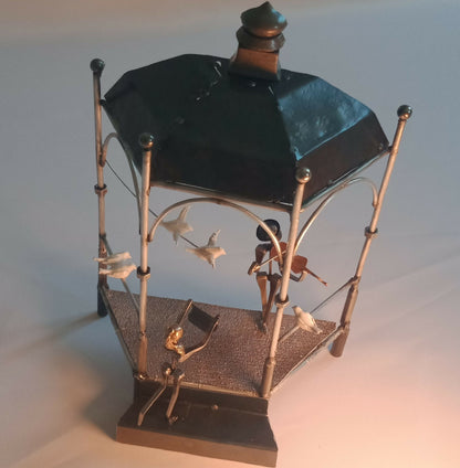 Cage de manège décorative en métal doré, vue en biais avec toit noir et figurines.