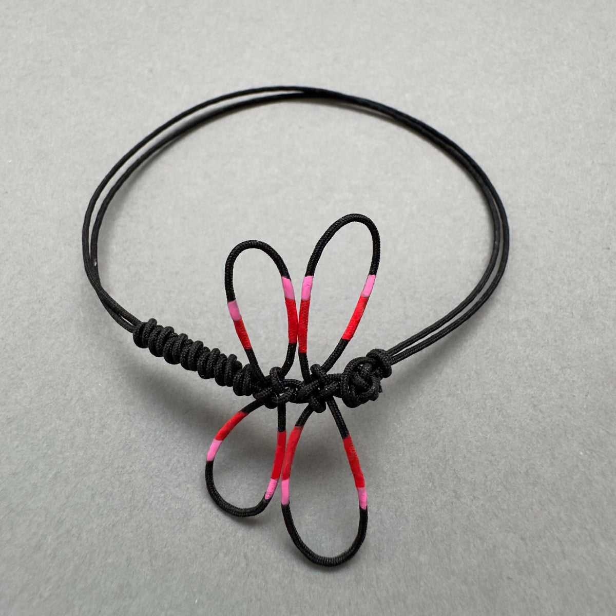 Bracelet noir en cordon tressé avec motif de libellule rose et rouge, vu de dessus.