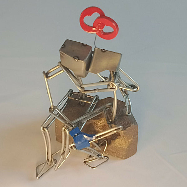 Sculpture en fils d’acier d’un couple sur socle, avec cœur rouge et détails bleus