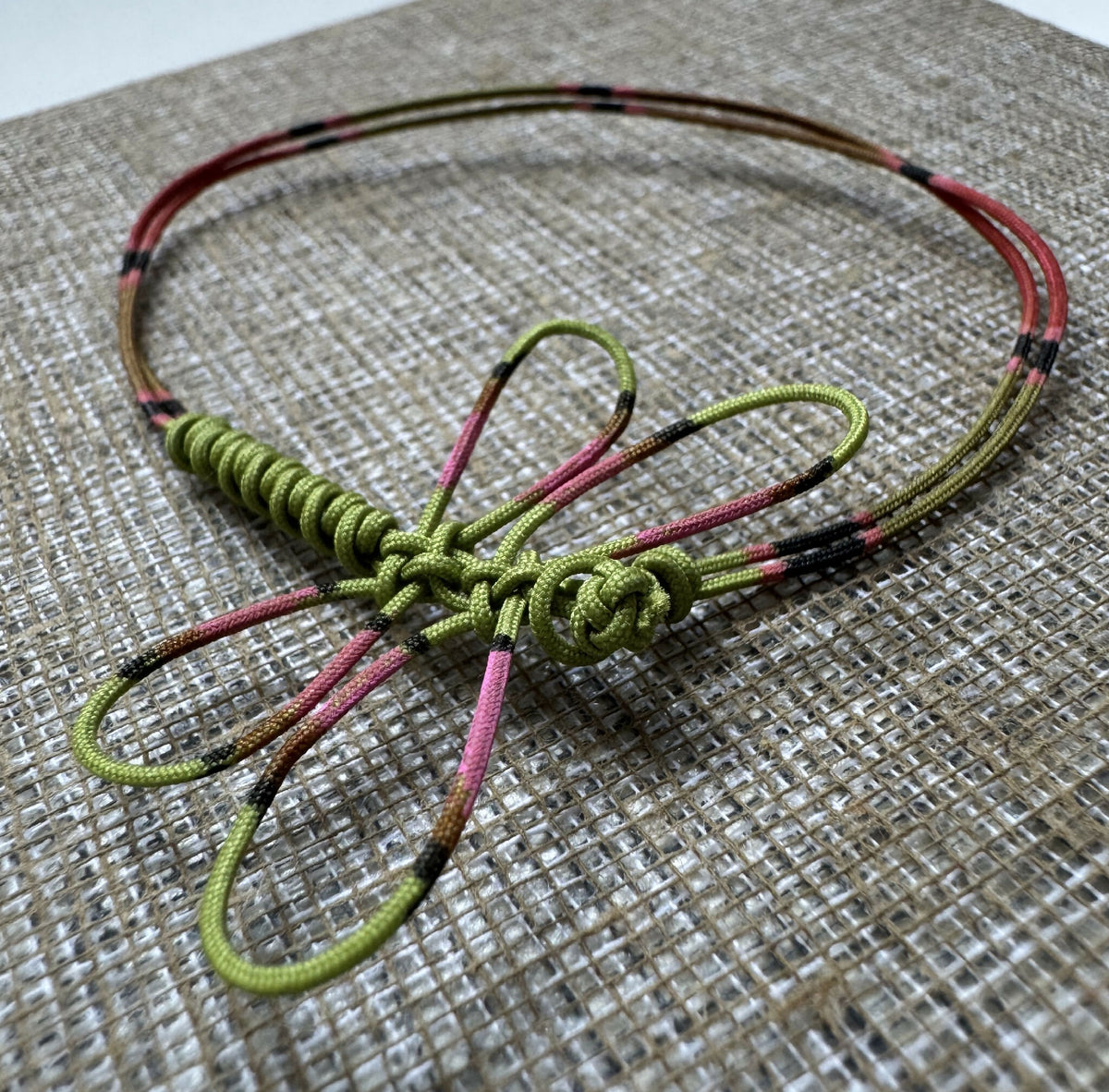 Bracelet cordon vert tressé avec libellule peinte rose/noire et attaches rouges et vertes.
