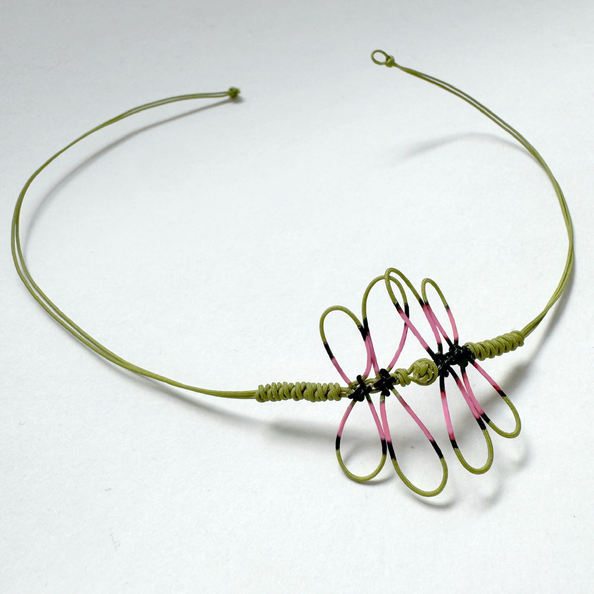 Bracelet fin cordon vert avec grande libellule peinte rose et noire sur nœud.