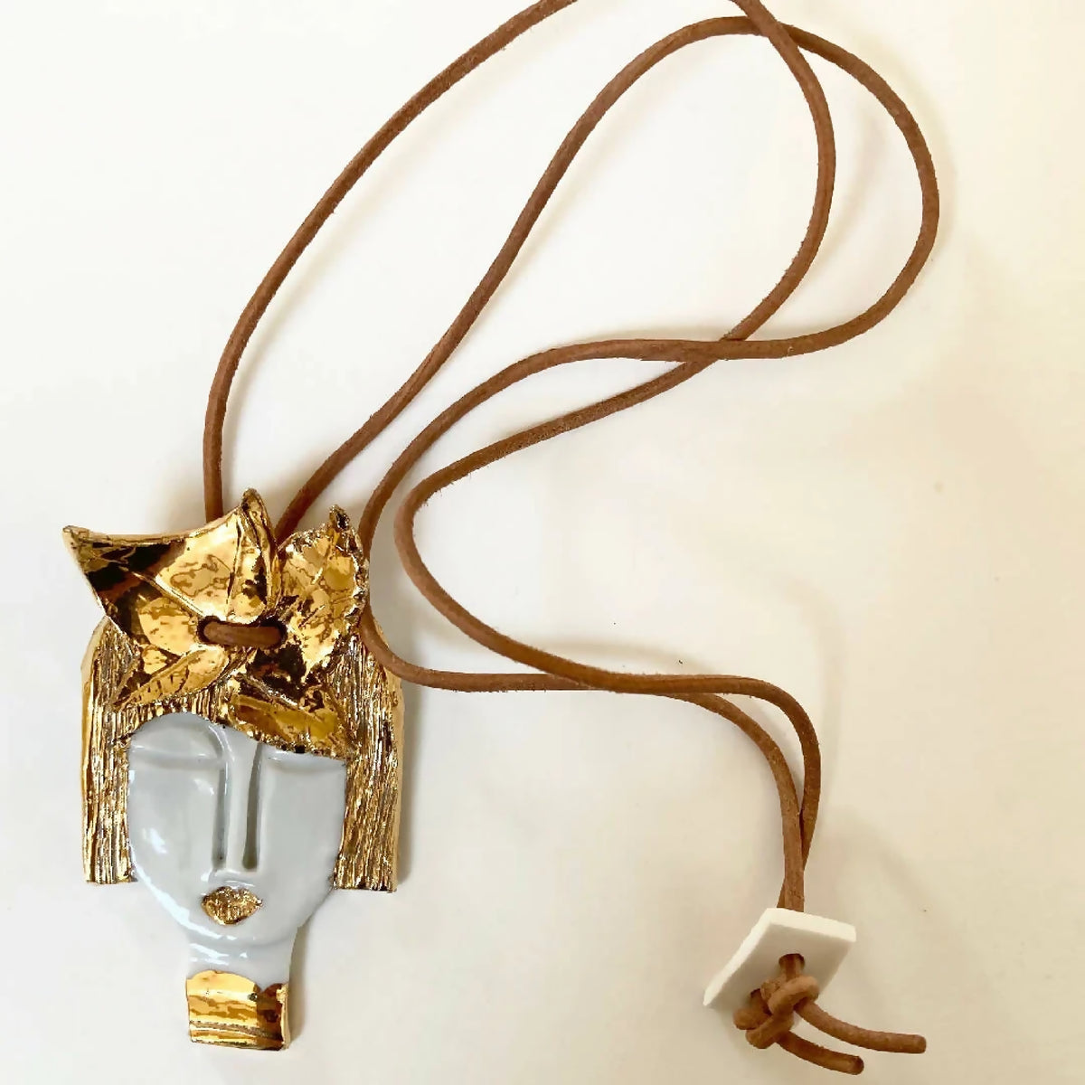 Pendentif visage d’Aphrodite, cordon brun noué, vue de côté