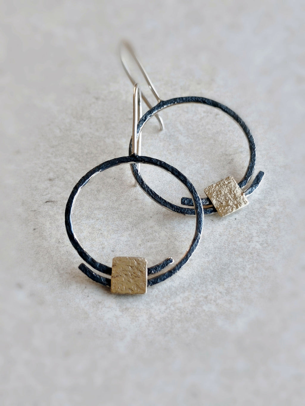Boucles d’oreilles pendantes : deux anneaux noirs et carrés dorés texturés, tiges argentées.