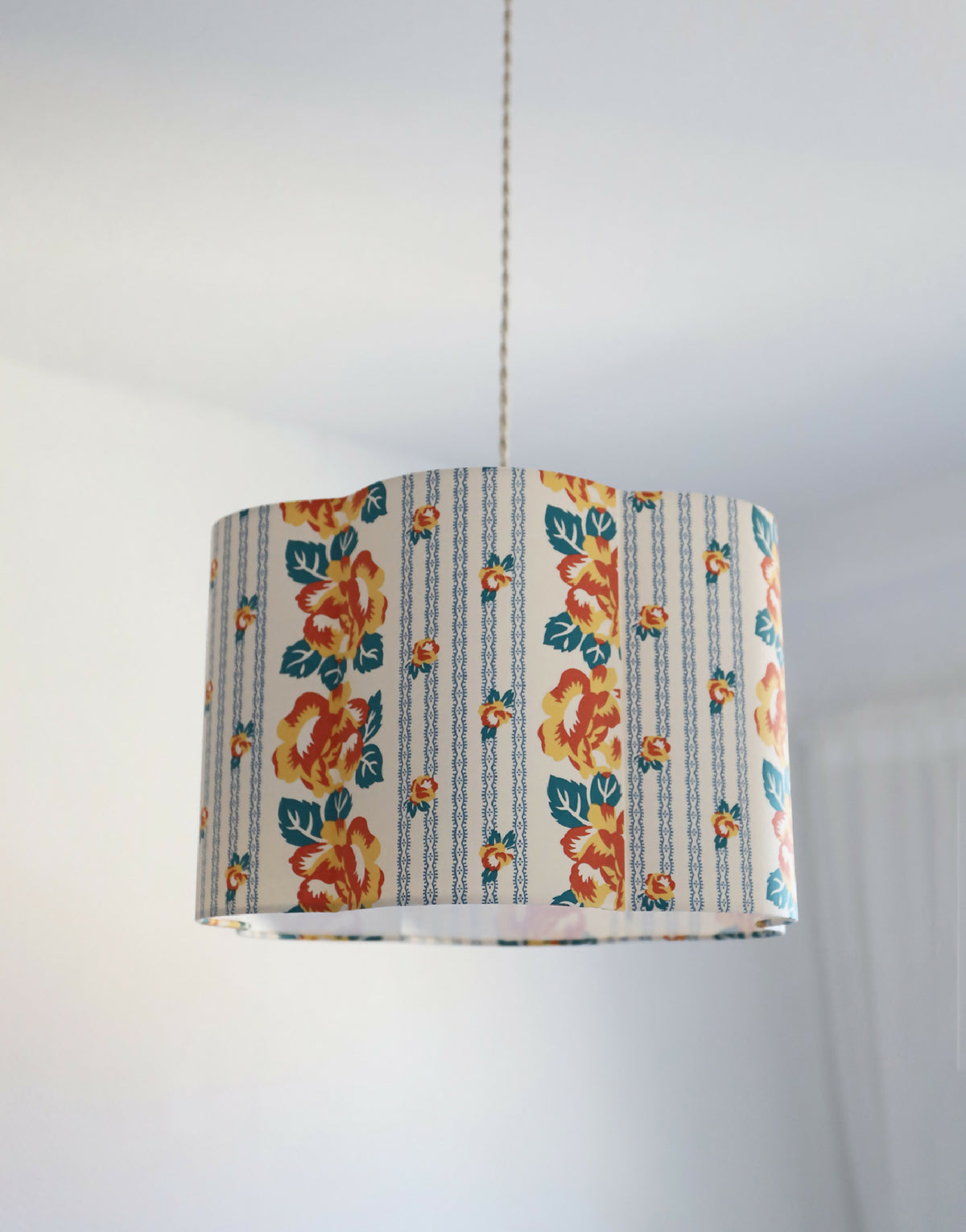 Abat-jour forme fleur en tissu bleu clair, motifs floraux orange, style rayures verticales.