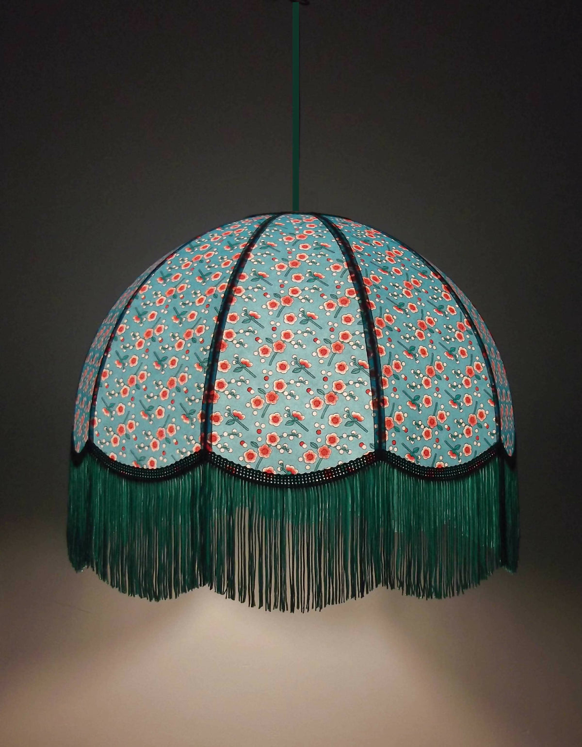 Suspension en papier bleu à motifs fleuris, franges vertes et liséré noir.