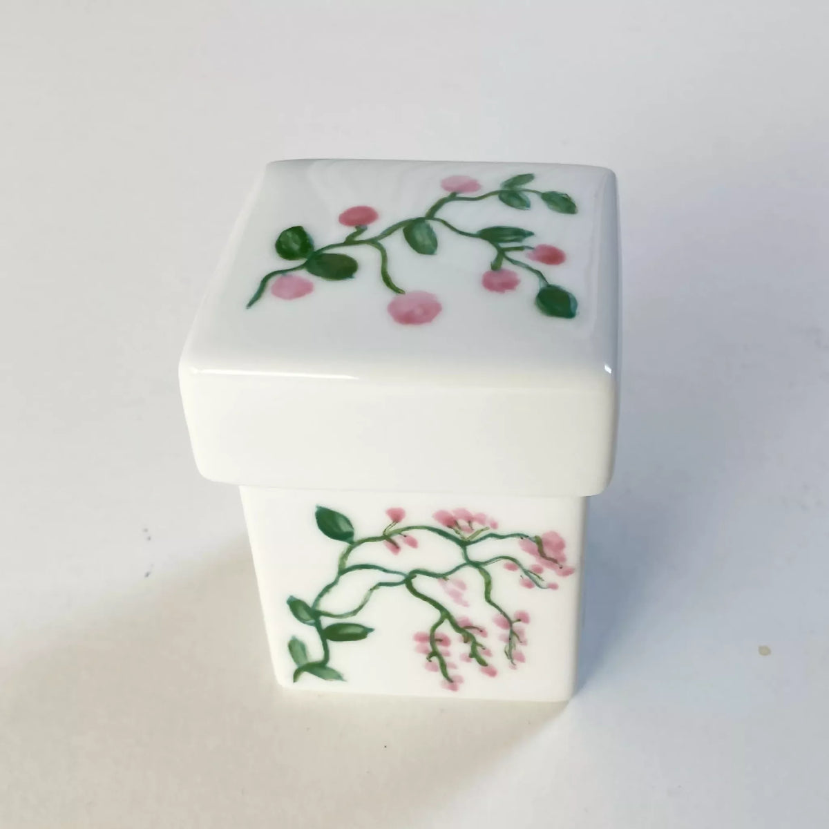 Boîte à bijoux en porcelaine blanche, motif floral rose et feuillage vert.