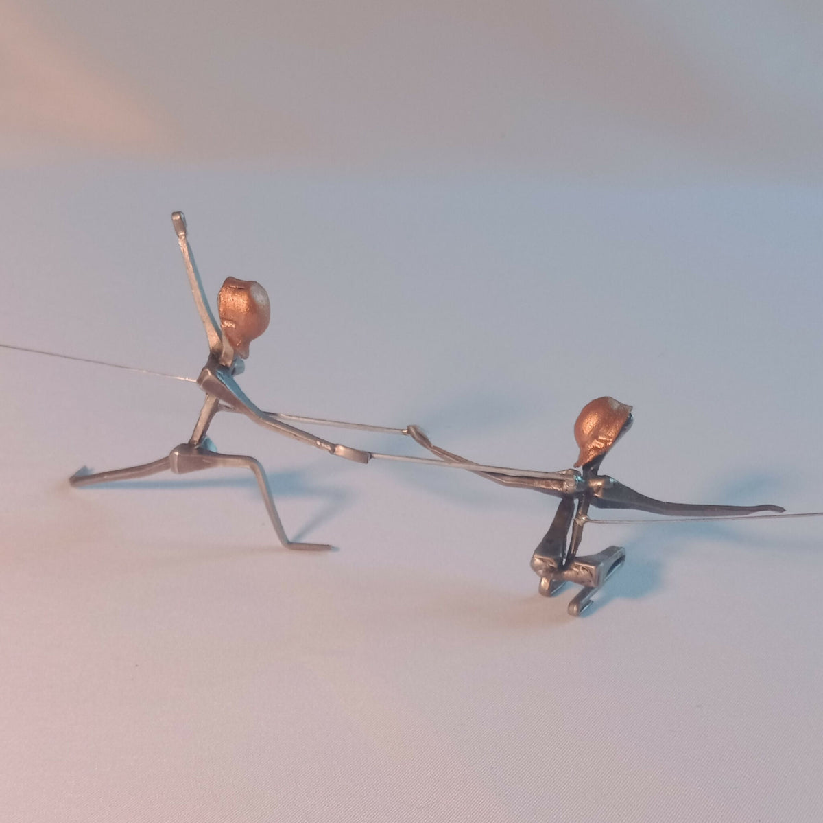Deux figurines d’escrimeuses en acier, corps bleu et têtes cuivre, bras en extension.