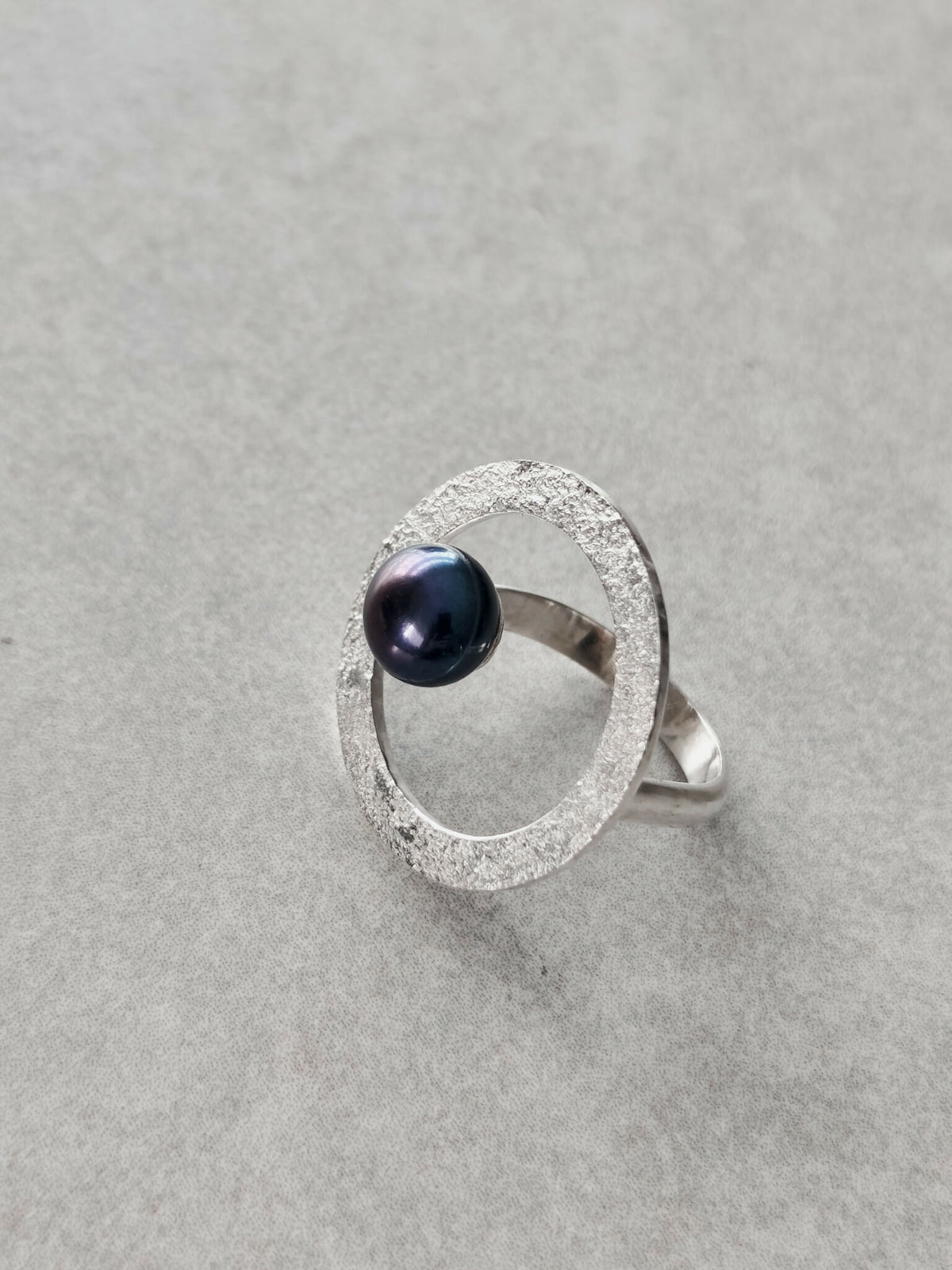 Bague argentée texturée en forme d’anneau ovale, cabochon bleu foncé visible de côté