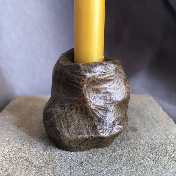 Mini bougeoir en pierre sombre avec bougie jaune, vue rapprochée.