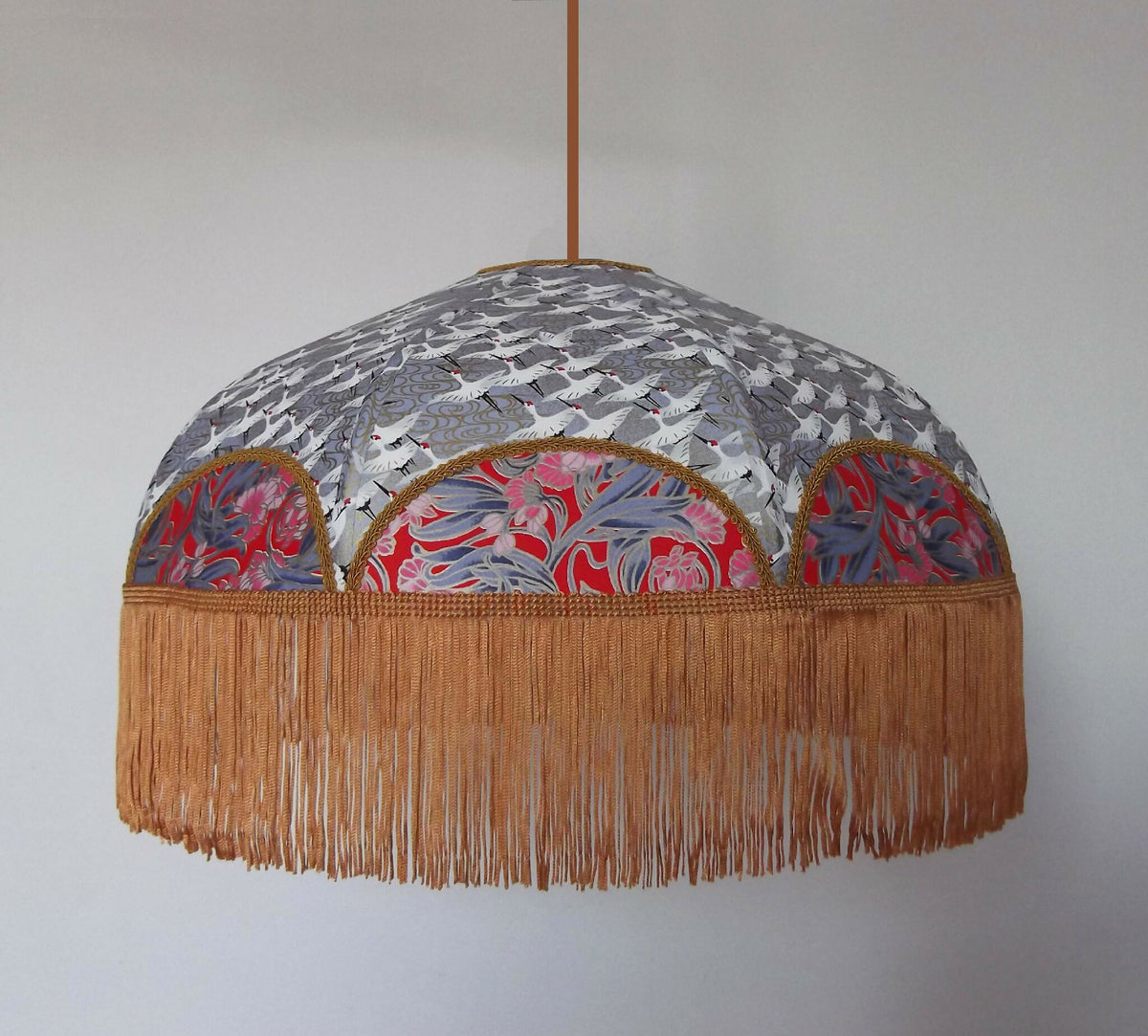 Suspension rétro : abat-jour rond gris à motifs japonais et franges dorées en bordure.