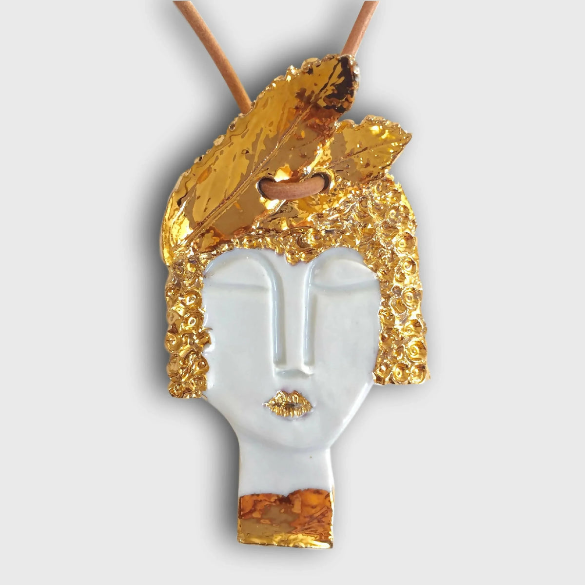 Pendentif visage féminin doré et blanc, détail yeux et bouche, attache pour cordon