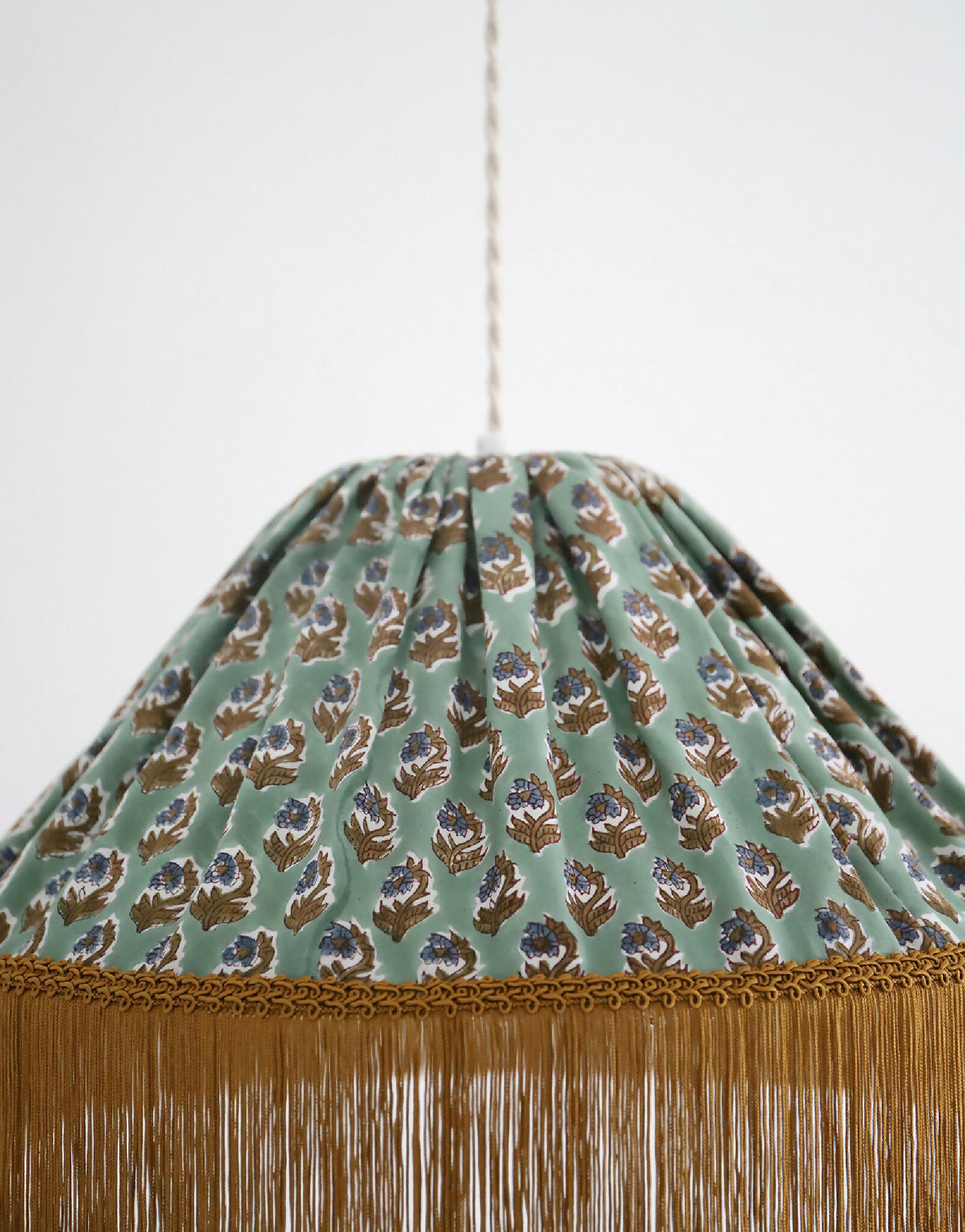 Détail de la suspension : tissu vert à motif floral et franges dorées sur la bordure.