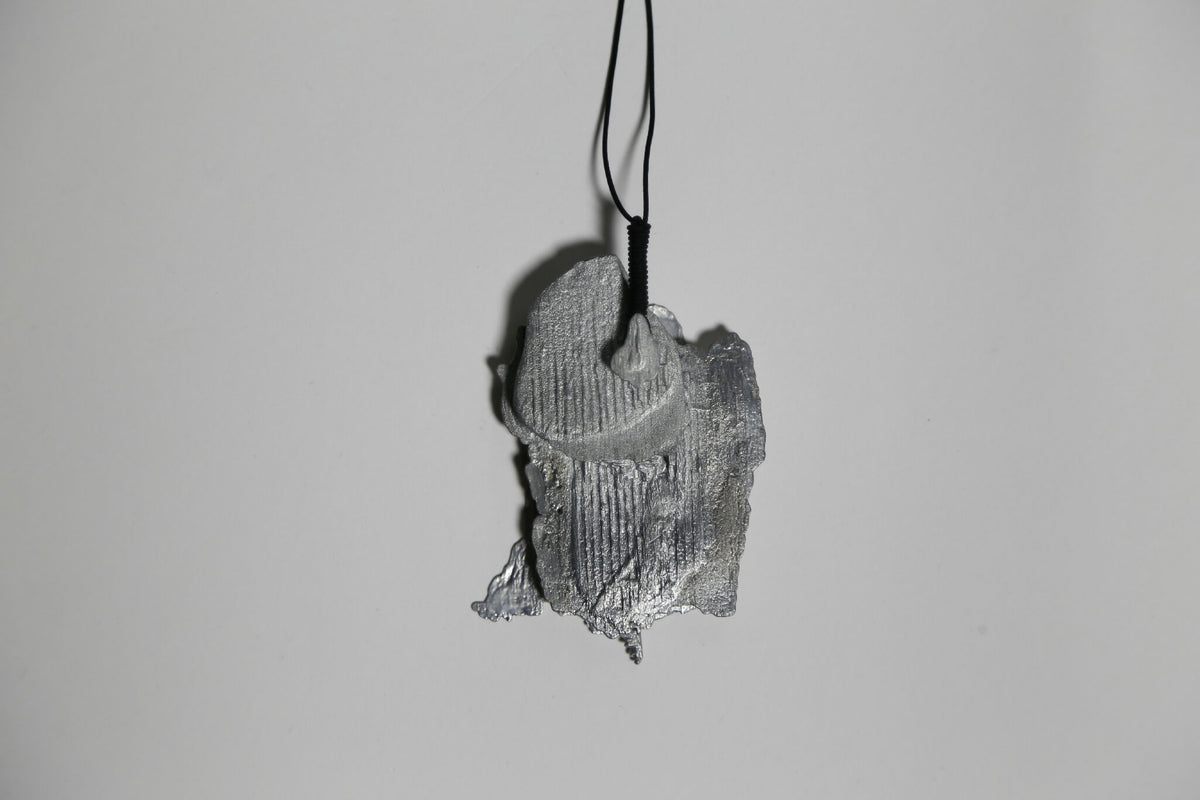 Pendentif gris en forme de feuille d’arbre, vue de trois-quarts, sur cordon.