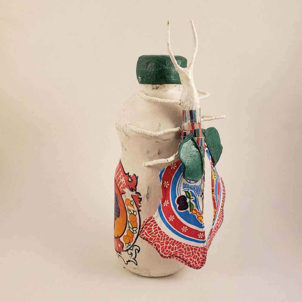 Sculpture posée sur une bouteille, vue de côté, corps blanc, capuchon vert, décor rouge et bleu