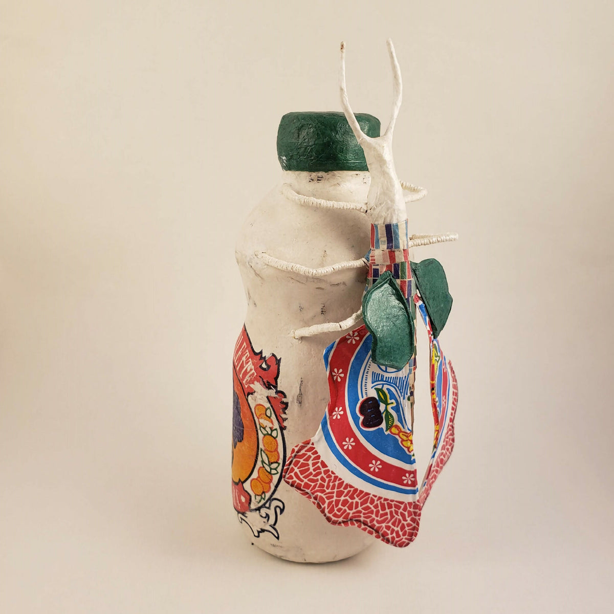 Sculpture posée sur une bouteille, vue de côté, corps blanc, capuchon vert, décor rouge et bleu