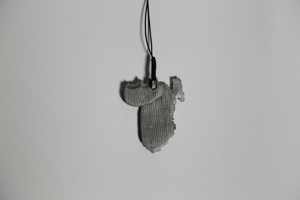 Pendentif gris en forme de feuille, vue de face, texture striée, sur cordon.