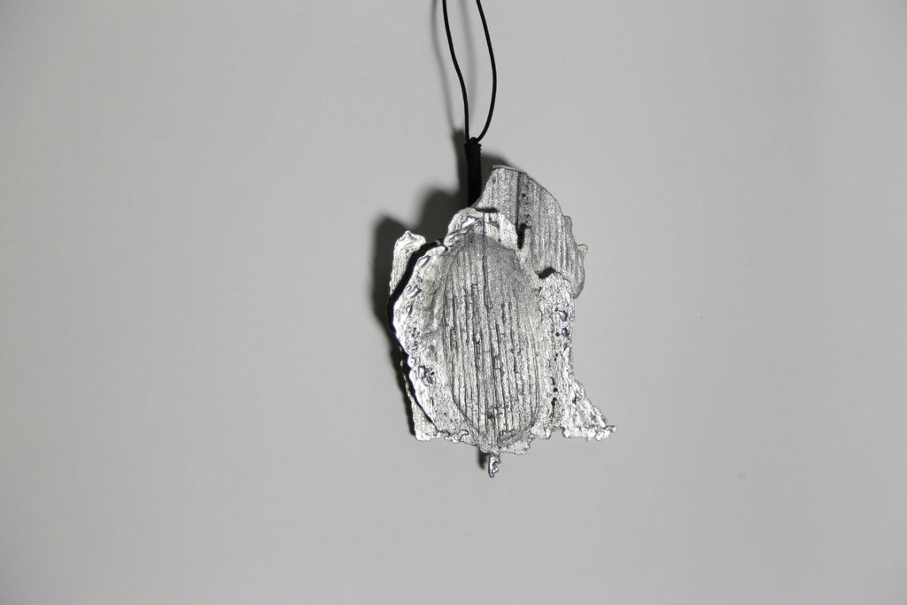 Pendentif argenté-gris en forme de feuille, vue rapprochée et inclinée, cordon noir.