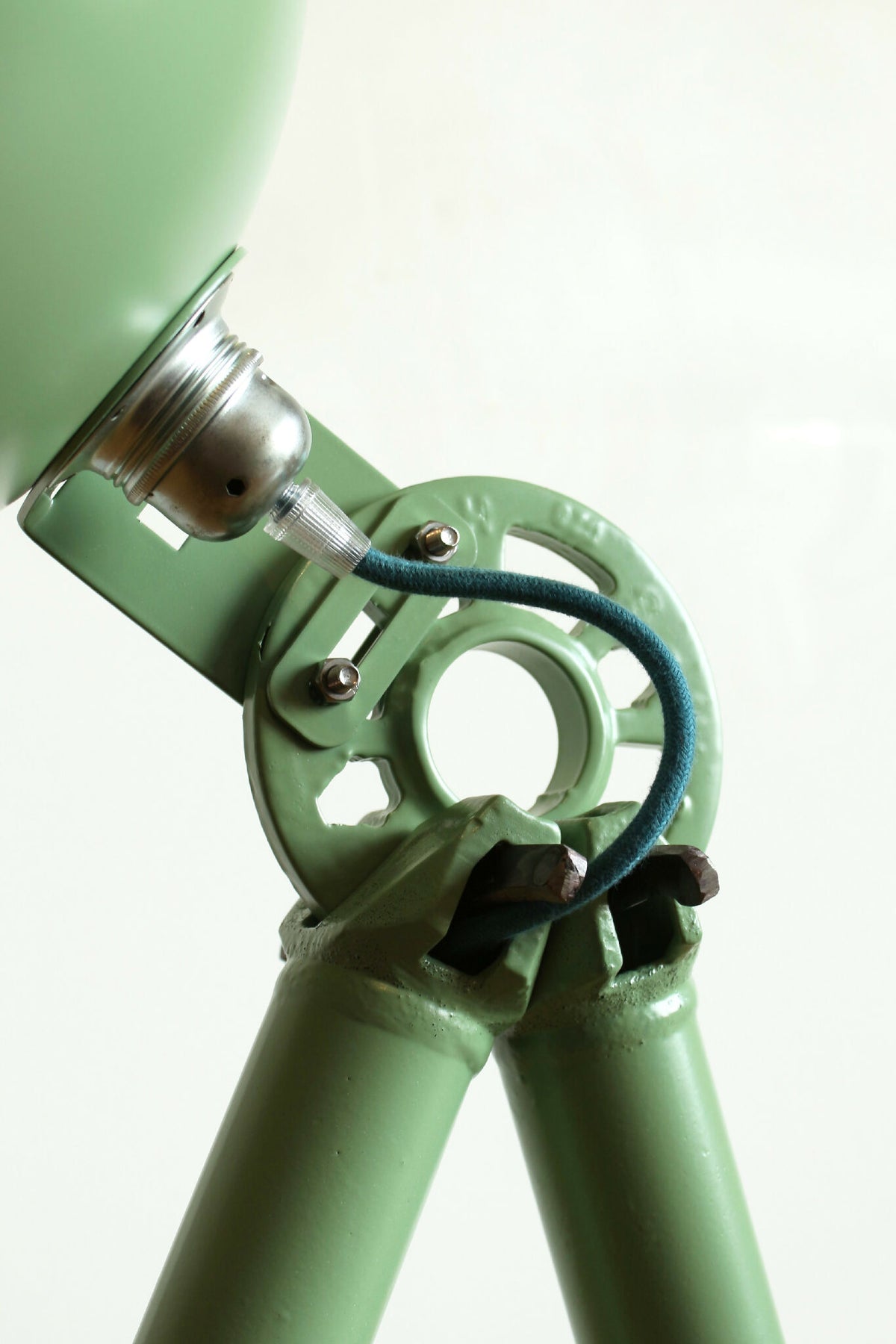 Lampe trépied vert, détail du mécanisme métallique et du câble bleu