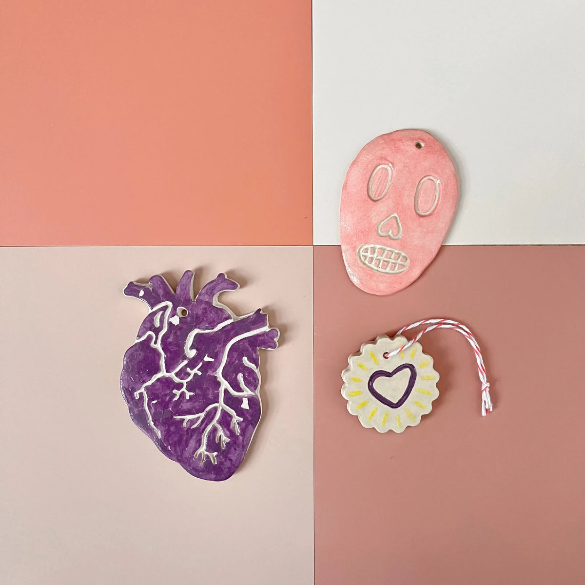Ex-votos en céramique : crâne rose, cœur anatomique violet et pendentif jaune au cœur
