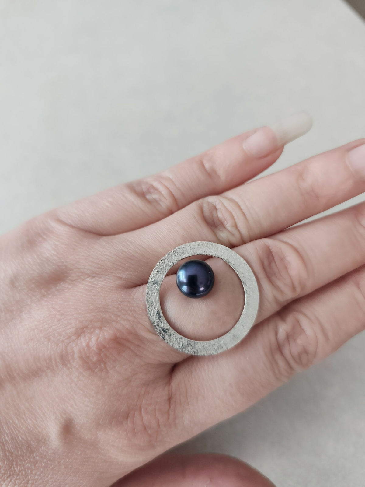 Bague ovale argentée texturée sur la main, cabochon bleu foncé au centre