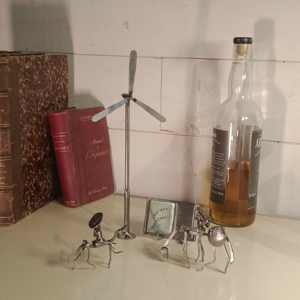 Ensemble décoratif en acier avec personnages miniatures, bouteilles et livres.