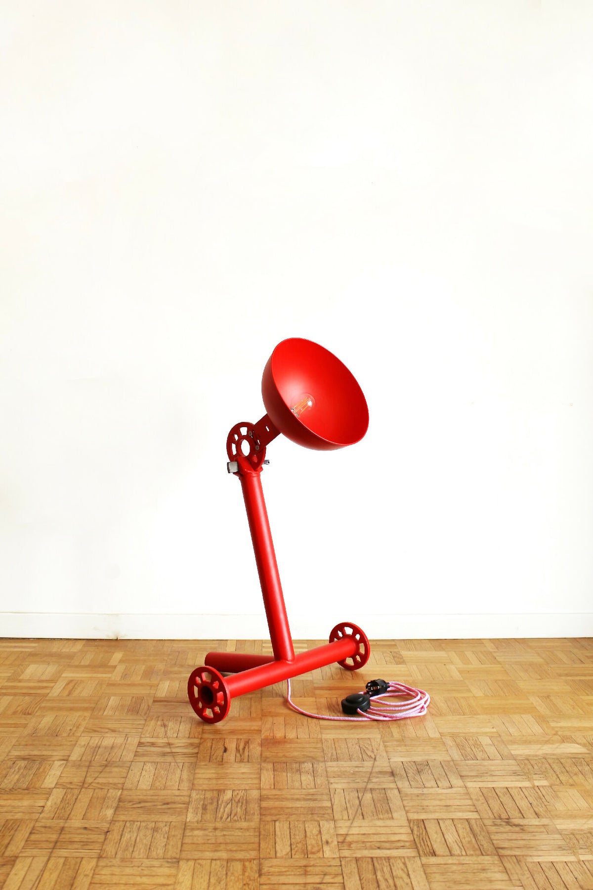 Lampe rouge sur trépied, abat-jour conique et cordon spiralé au sol