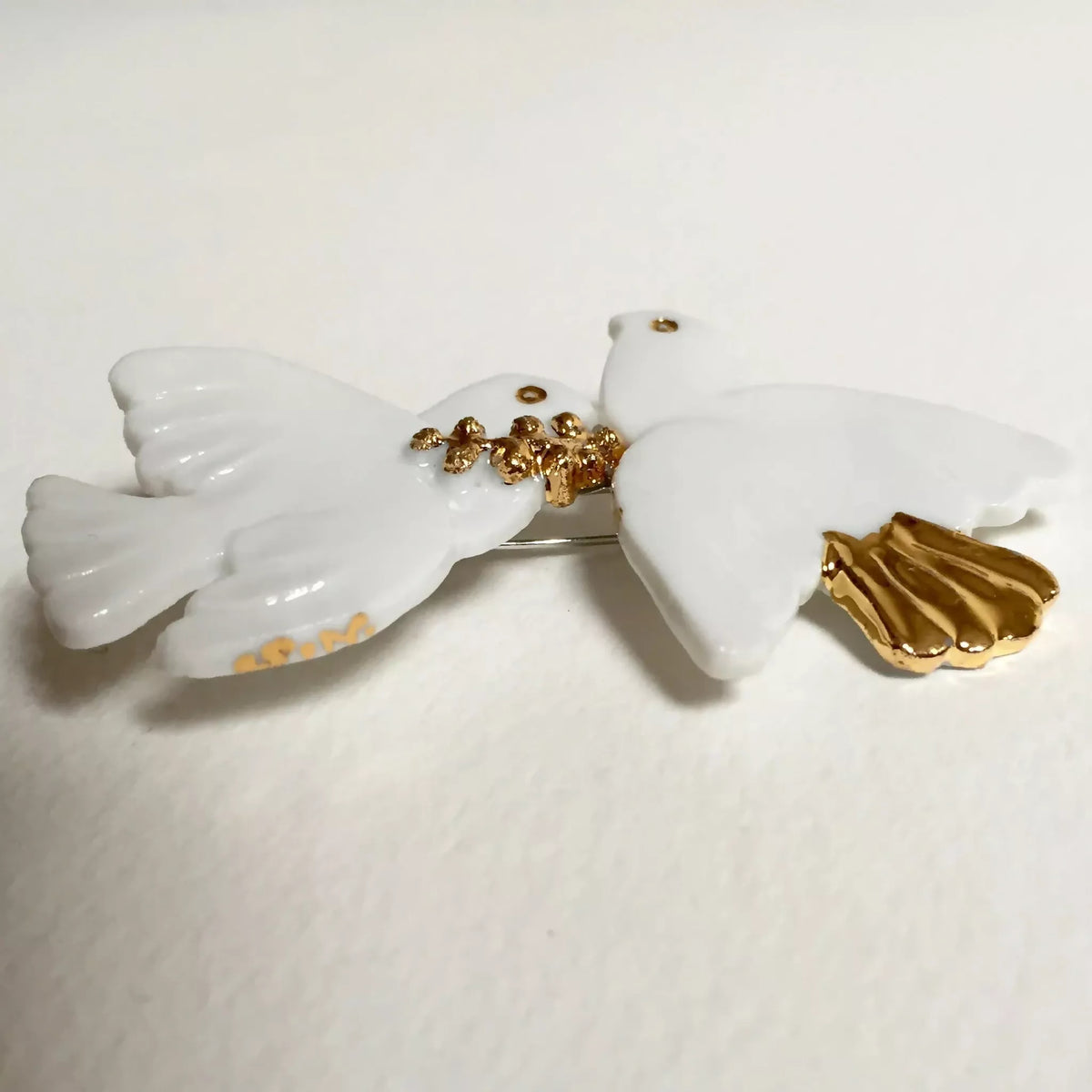 Broche colombes blanches, motif doré au centre et épingle arrière visible.