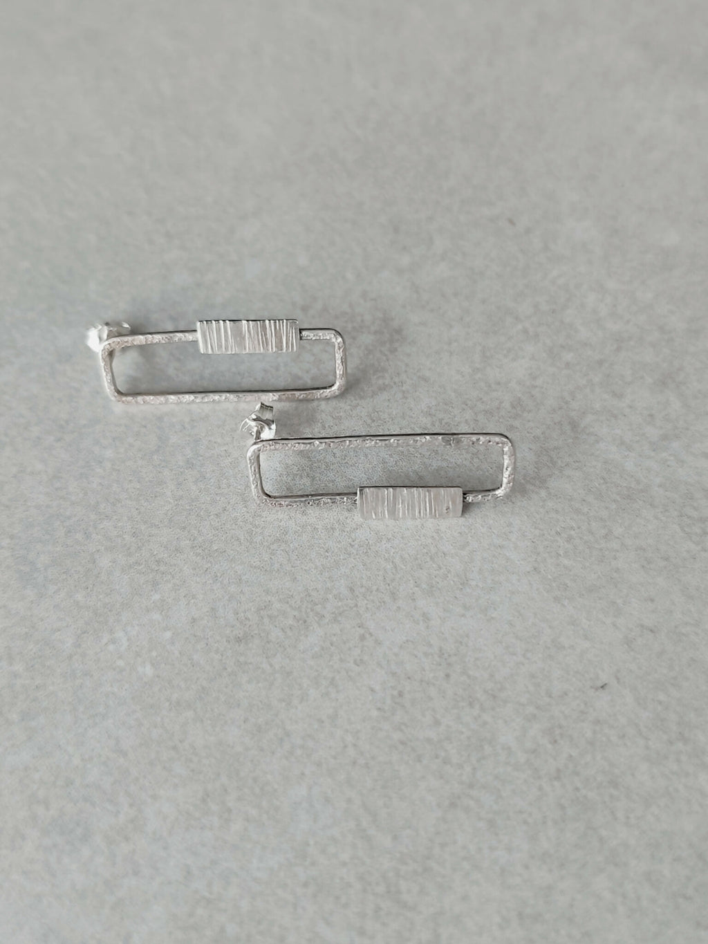 Boucles d’oreilles rectangulaires argentées, détail des fermoirs et des rayures.