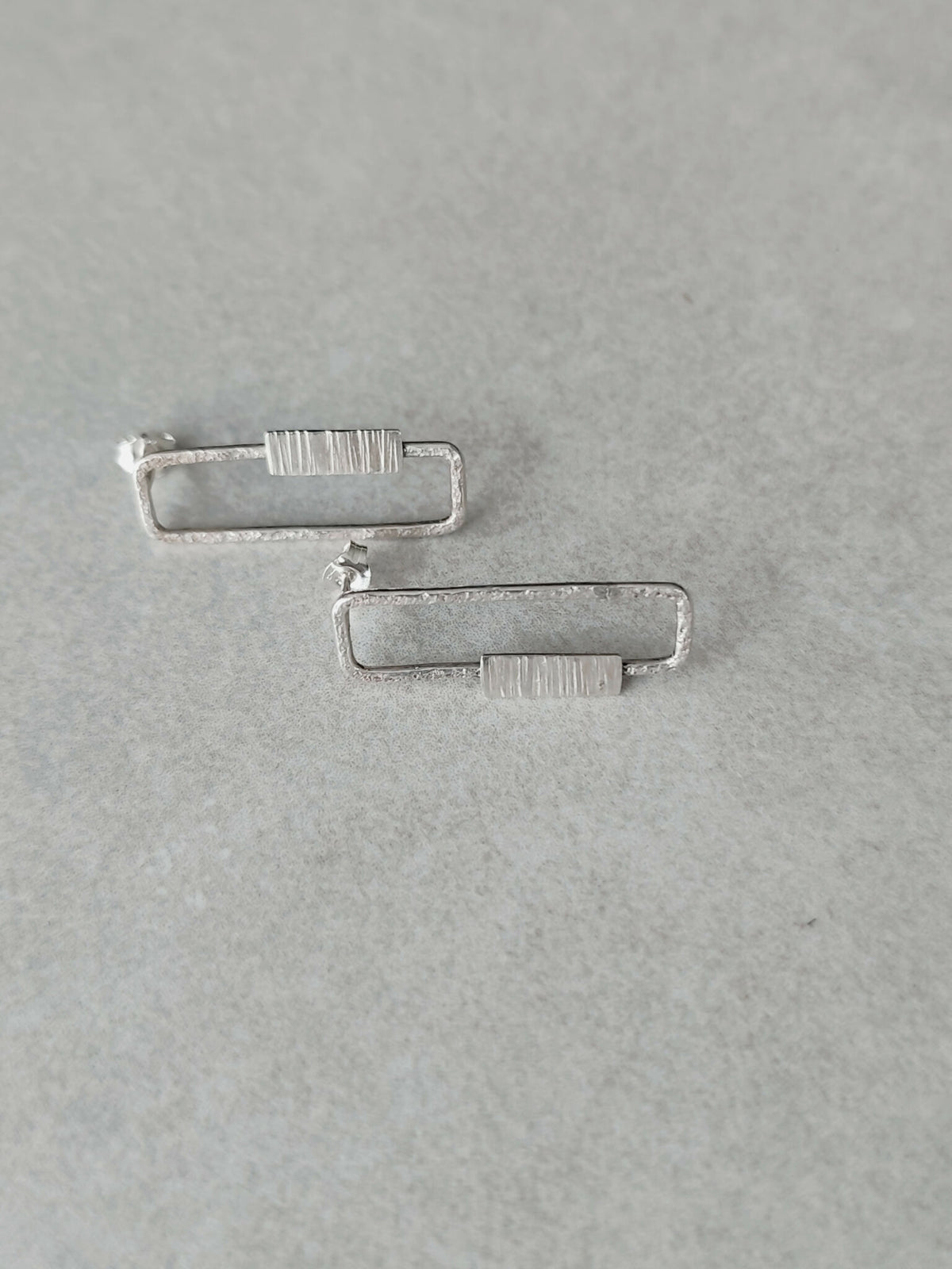 Boucles d’oreilles rectangulaires argentées, détail des fermoirs et des rayures.