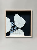 Tableau en relief avec formes blanches sur fond bleu foncé, cadre en bois clair