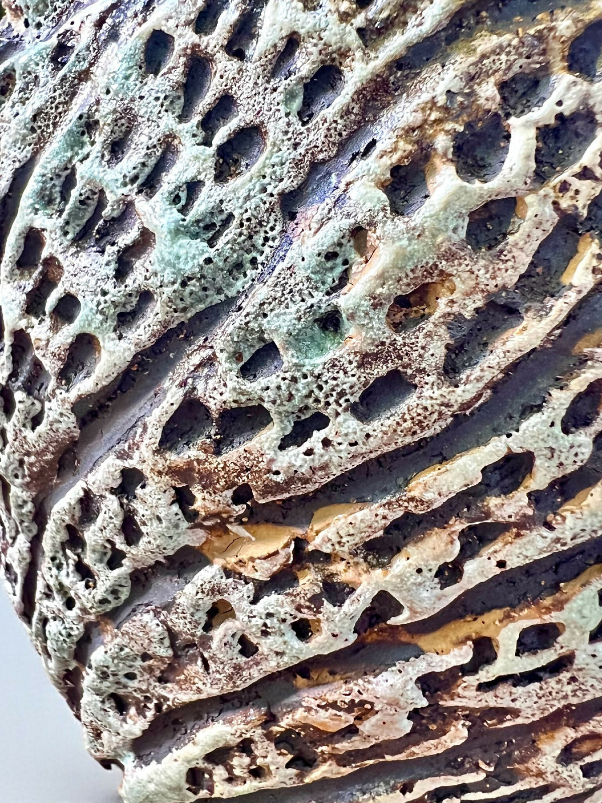 Gros plan sur pot en grès sculpté, surface texturée bleu-vert et sombre