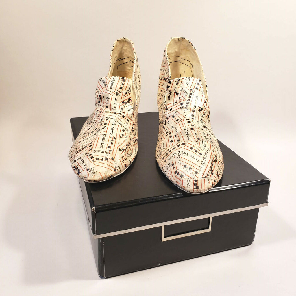 Escarpins beige à motif imprimé, posés sur boîte noire, semelles visibles.