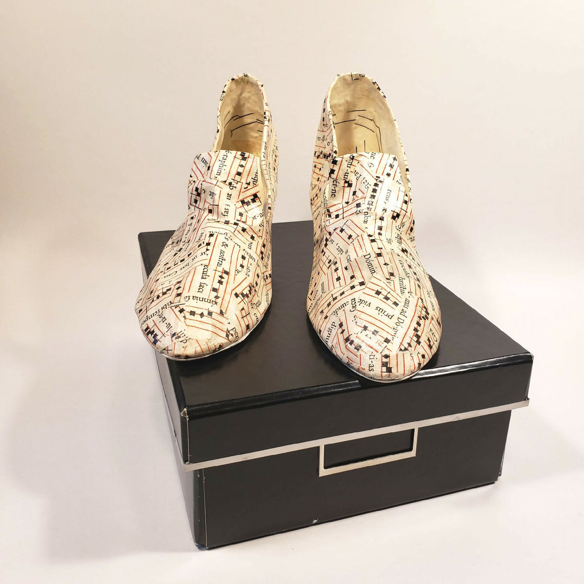 Escarpins beige à motif imprimé, posés sur boîte noire, semelles visibles.