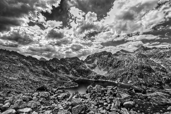 Lac de Migouélou, eau calme entourée de montagnes rocheuses et ciel nuageux
