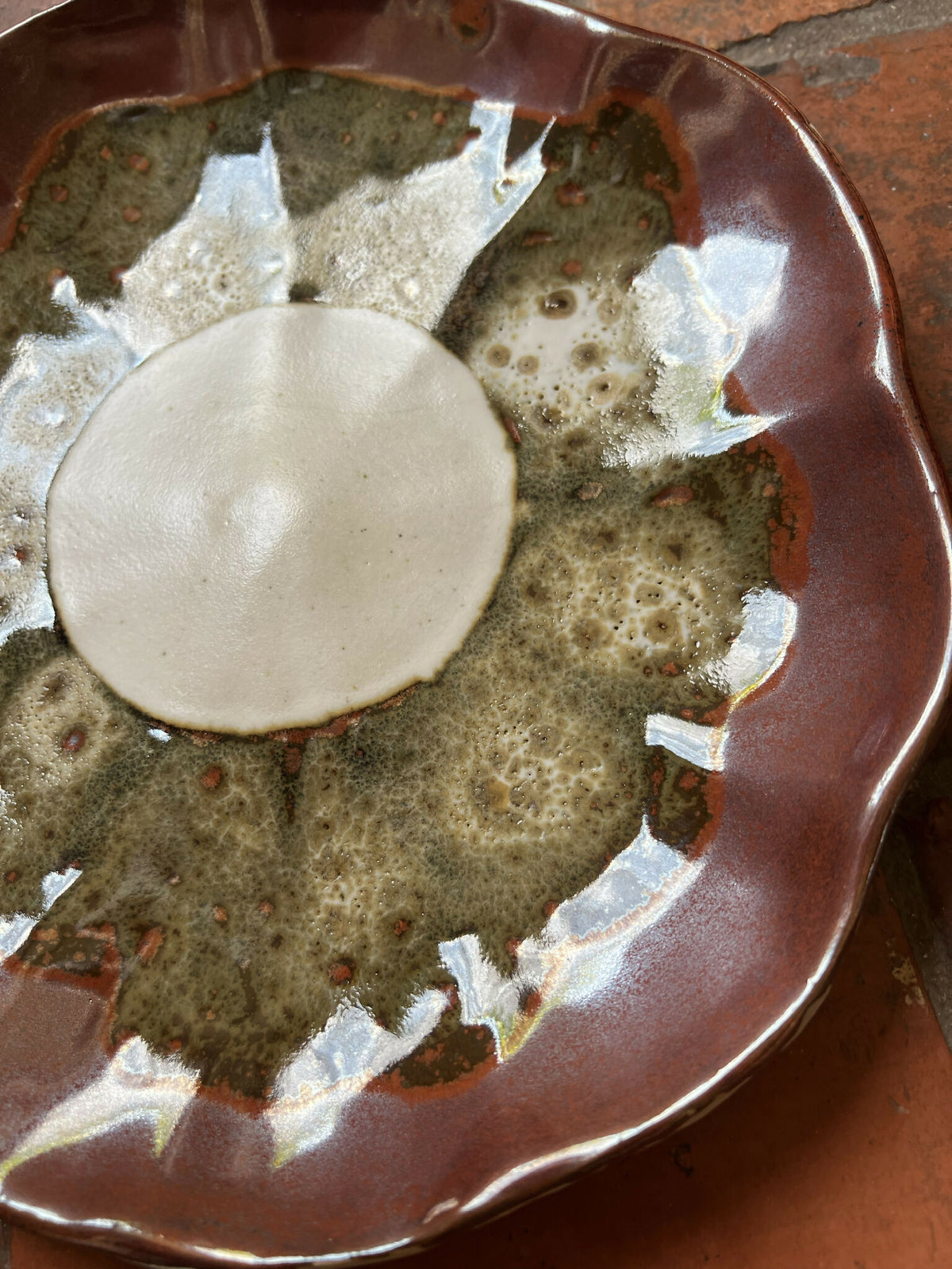 Assiette Prunelle bord brun, vue rapprochée : décor vert moucheté avec points rouges.
